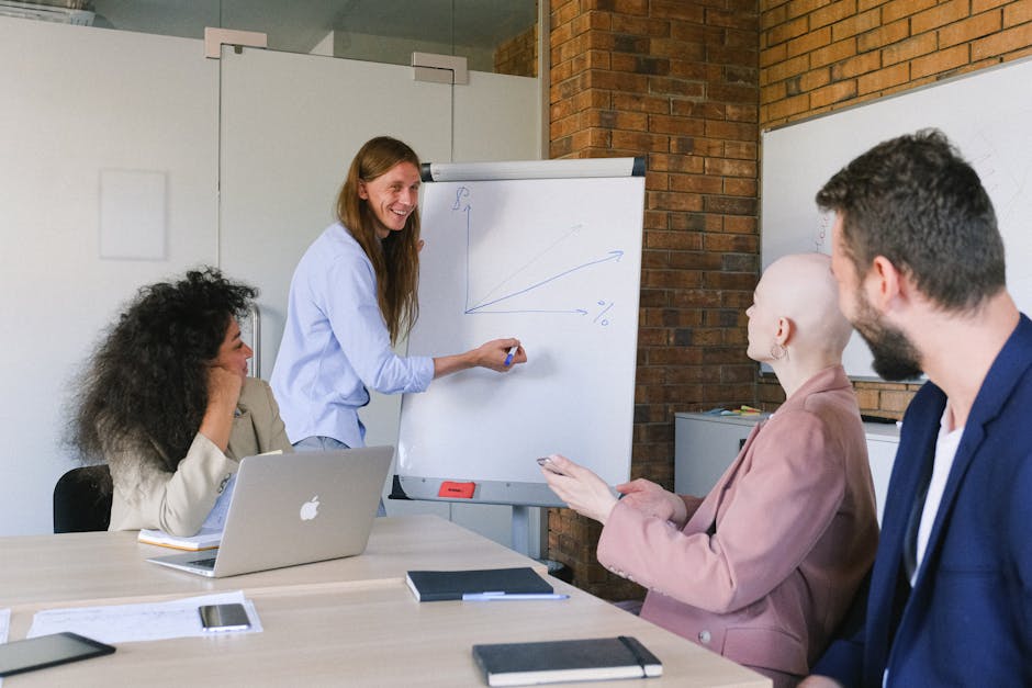 Smiling speaker drawing graph on  whiteboard while explaining details of project to coworkers in modern workspace in daytime
